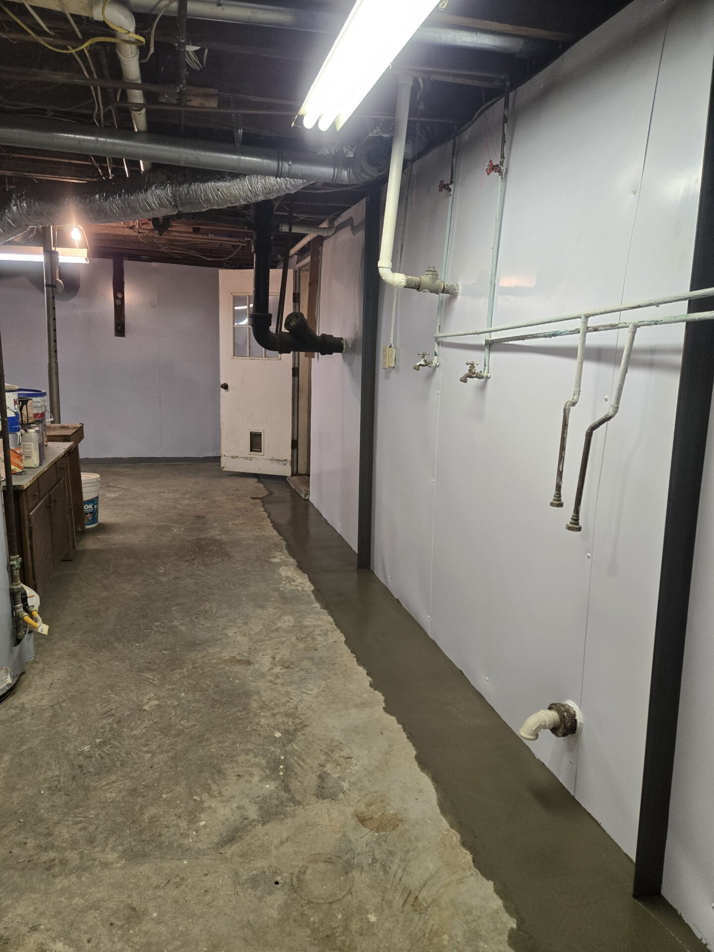 Unfinished basement with exposed pipes and fluorescent lights